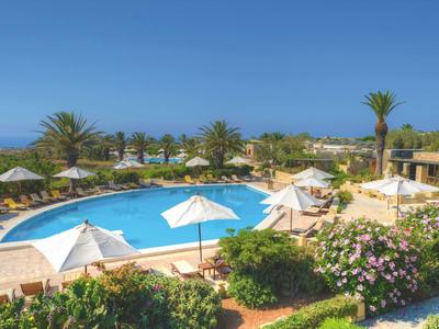 Großer Pool mit Sonnenschirmen und Palmen in einer Hotelanlage bei klarem Himmel.