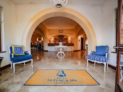 Luminoso vestíbulo de hotel con dos sillones azules y una alfombra con el logo del hotel y spa.