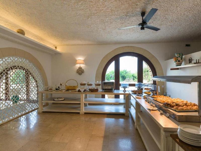 Sala de desayuno luminosa con buffet, mesas de madera y grandes ventanas arqueadas con vista a la vegetación.