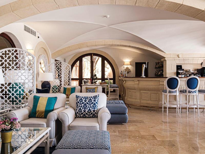 Salón luminoso con muebles blancos, acentos azules y barra en un hotel elegante.