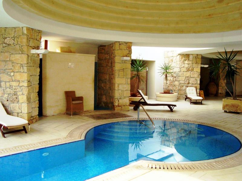 Piscina interior con forma curva, rodeada de tumbonas y paredes de piedra natural.