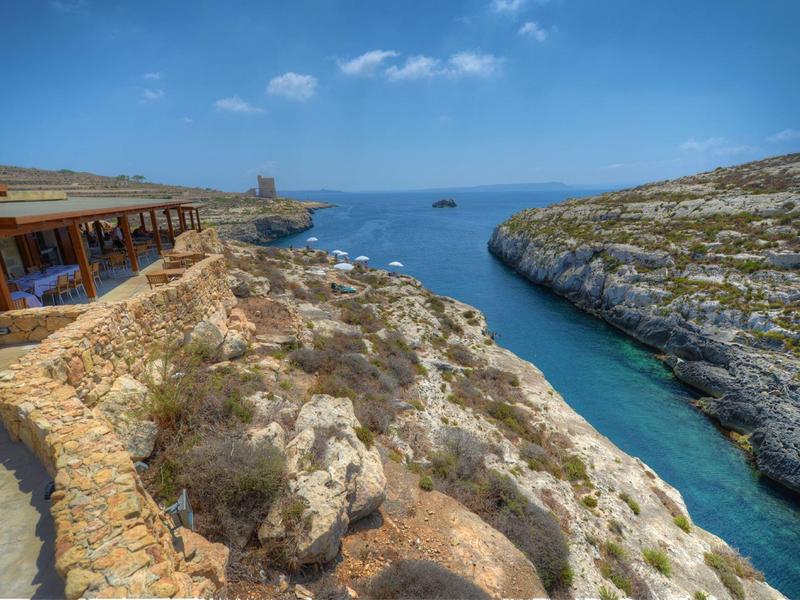 Acantilados con agua azul clara y un camino de piedra junto a un edificio junto al mar.