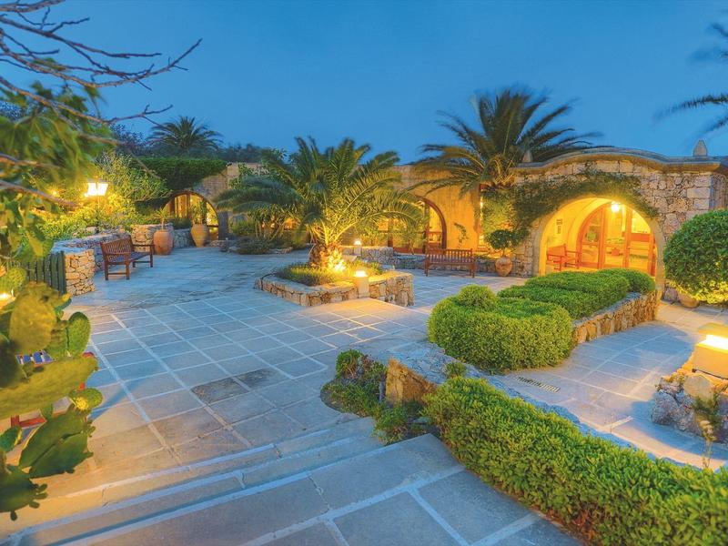 Jardín mediterráneo iluminado de hotel con palmeras y sendero pavimentado al atardecer