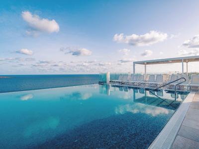 Infinity-Pool mit Meerblick und Sonnenliegen unter blauem Himmel
