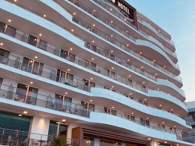 Edificio hotelero moderno con balcones curvos y fachada iluminada bajo cielo azul claro.