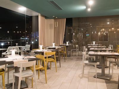 Moderní restaurace s bílými a žlutými židlemi s výhledem na město v noci.