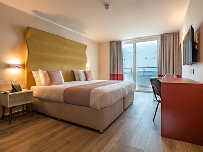 Moderní hotelový pokoj s manželskou postelí, balkonem a výhledem na moře.