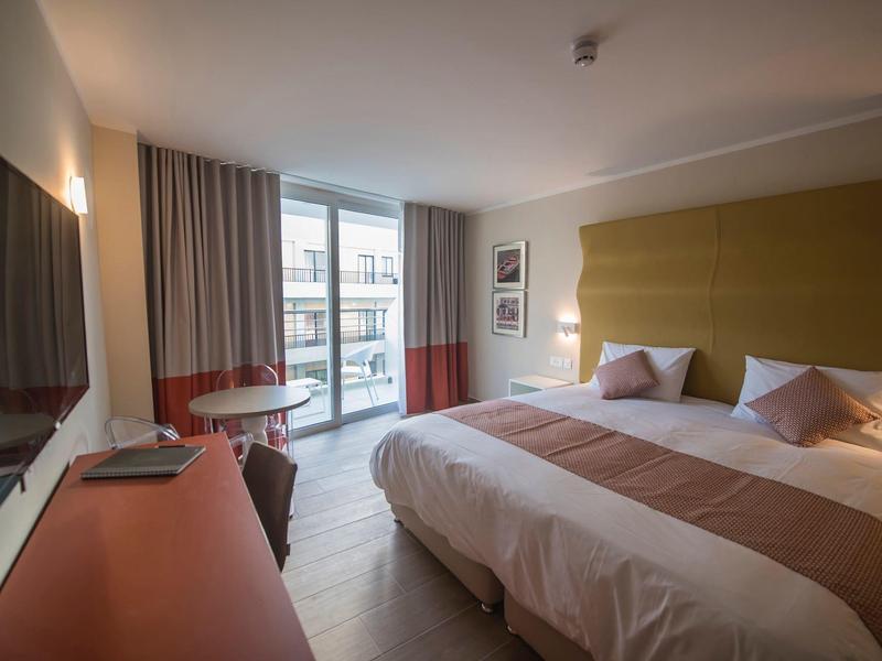 Moderní hotelový pokoj s velkou postelí, TV a balkonem s výhledem.