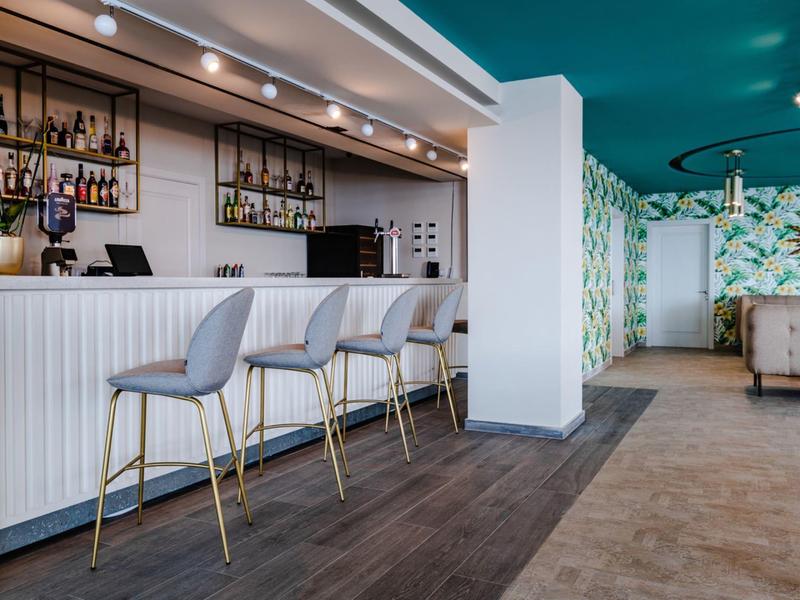 Moderní hotelový bar s barovými židličkami, světlými stěnami a stylovým osvětlením.