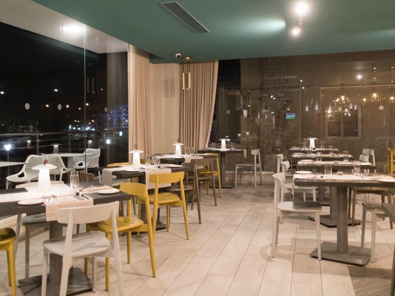 Moderní restaurace s bílými a žlutými židlemi s výhledem na město v noci.