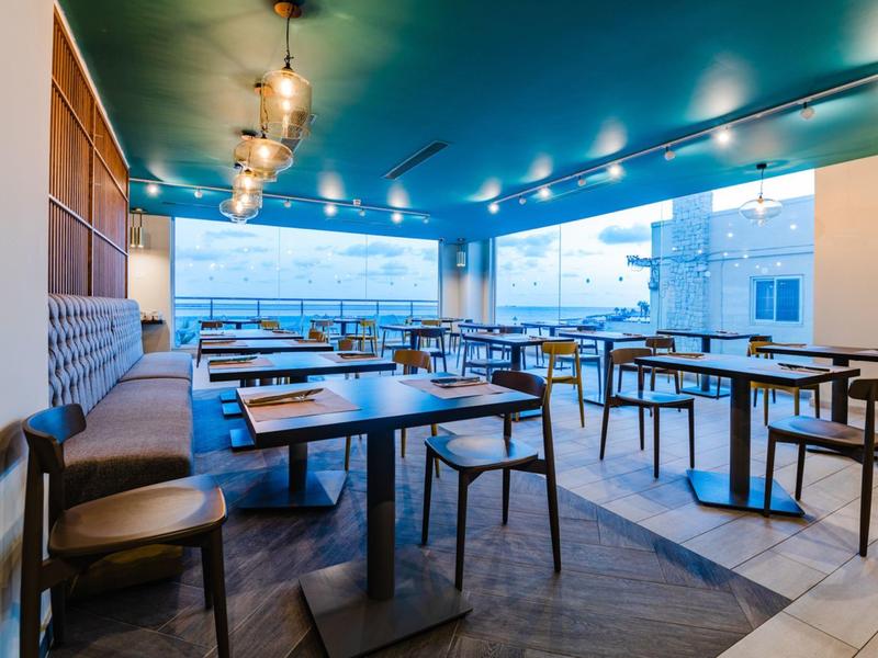 Moderní venkovní část hotelové restaurace s stoly a židlemi při západu slunce.