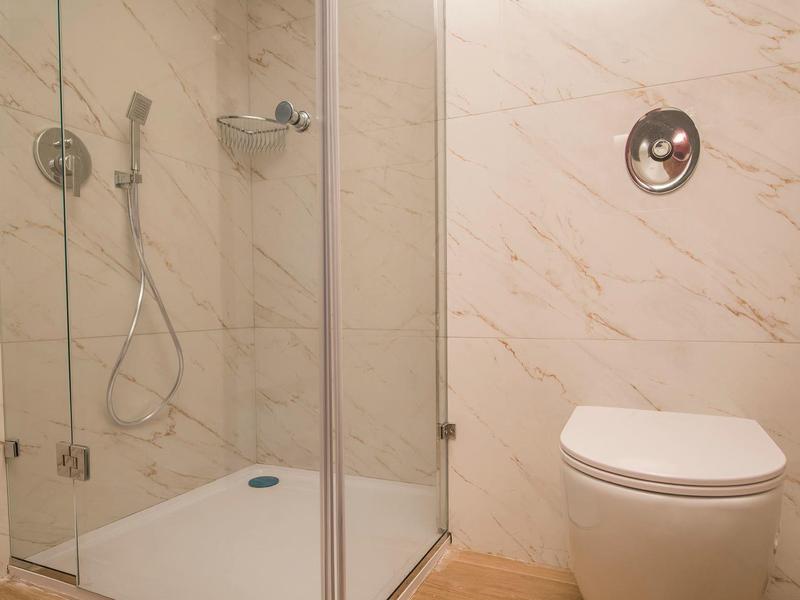 Moderní koupelna se skleněným sprchovým koutem a závěsným WC v neutrálních béžových a bílých tónech.