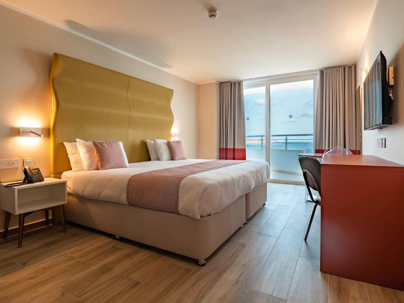 Moderní hotelový pokoj s manželskou postelí, balkonem a výhledem na moře.
