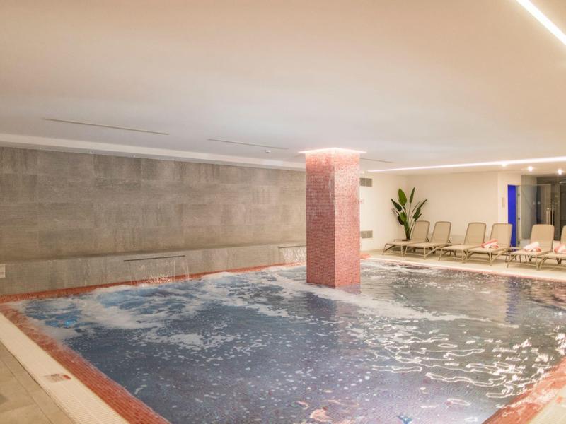 Moderní vnitřní bazén s bublinkovou zónou ve stylovém wellness prostoru.