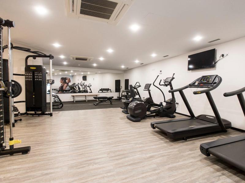 Moderní posilovna s běžeckými pásy, rotopedy a posilovacími stroji v jasné místnosti.
