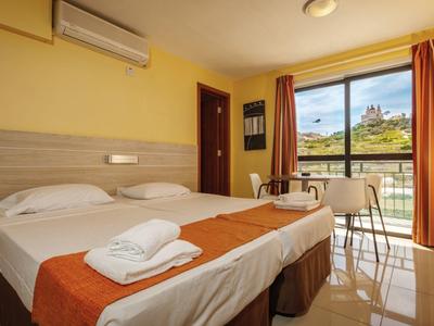 Una habitación de hotel luminosa con dos camas, cortinas naranjas y vista a un paisaje verde.