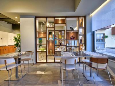 Área de comedor moderna con estantes, mesas, sillas y grandes ventanas.