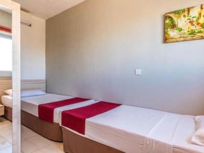 Habitación de hotel sencilla con dos camas individuales, corredores rojos y un cuadro en la pared.