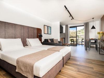 Habitación de hotel moderna con dos camas individuales, zona de estar y balcón con vista a la montaña.