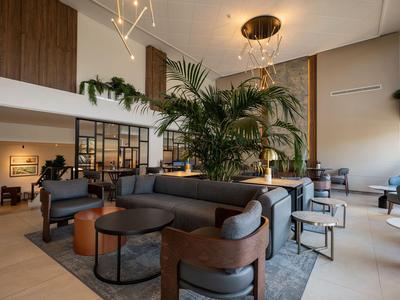Moderní hotelová lounge s křesly, pohovkami, stolky a velkými rostlinami v otevřeném prostoru.