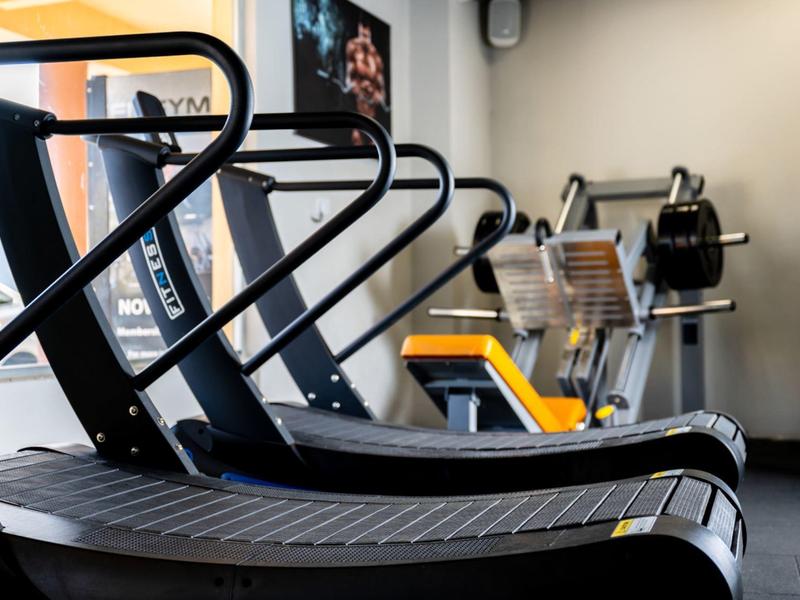 Varias cintas de correr en un gimnasio moderno con paredes claras y luz natural de la ventana.
