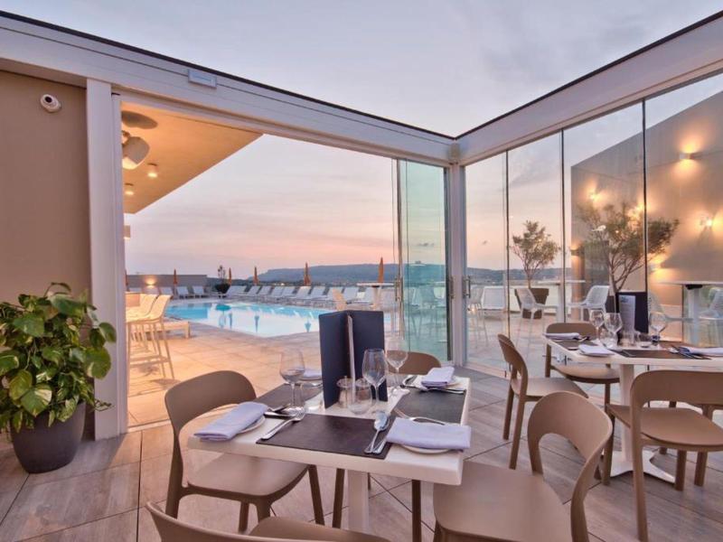 Restaurante moderno con paredes de vidrio con vistas al puerto al atardecer.