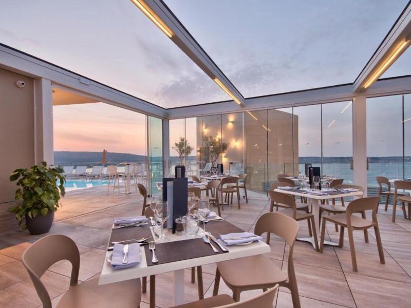 Restaurante moderno al aire libre con paredes de vidrio y vista a la ciudad al atardecer.