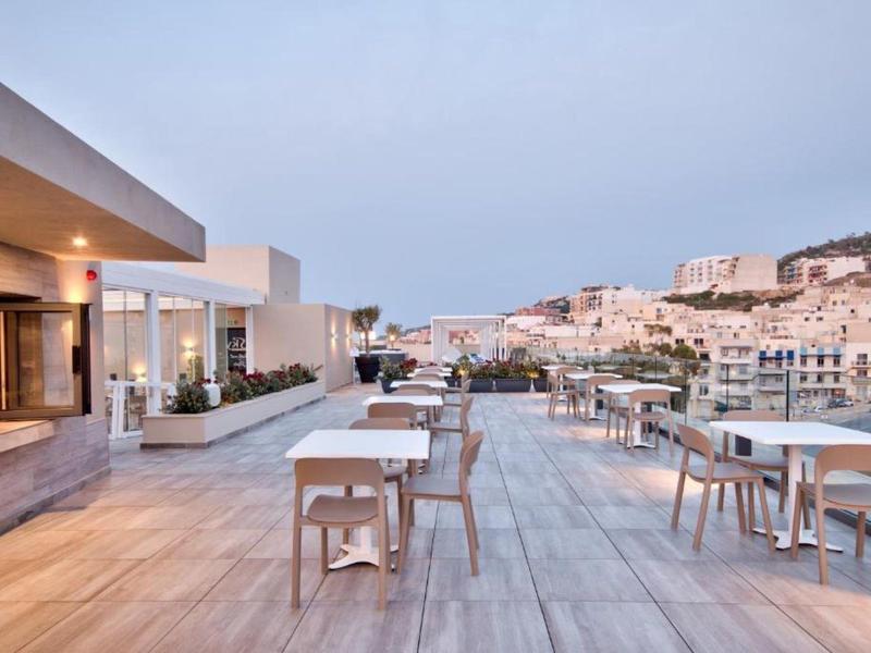 Terraza exterior moderna con mesas y sillas con vistas a la ciudad al atardecer.