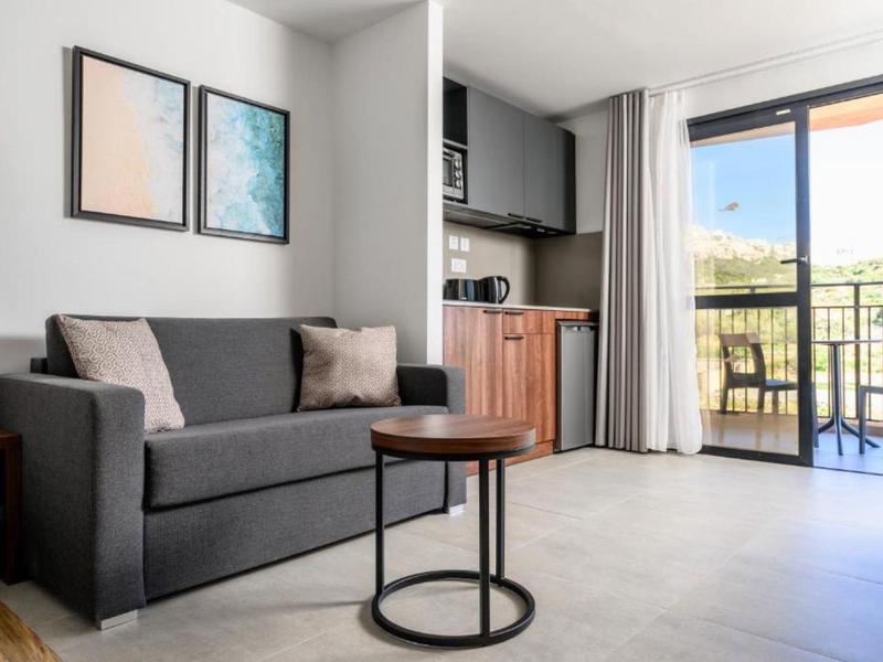 Sala moderna con sofá gris, mesa pequeña y acceso a balcón con vista.