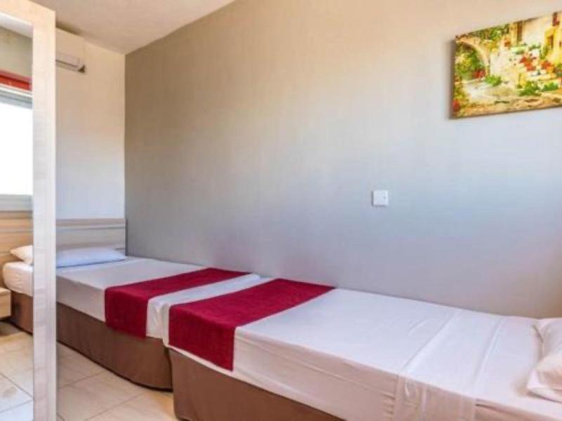 Habitación de hotel sencilla con dos camas individuales, corredores rojos y un cuadro en la pared.