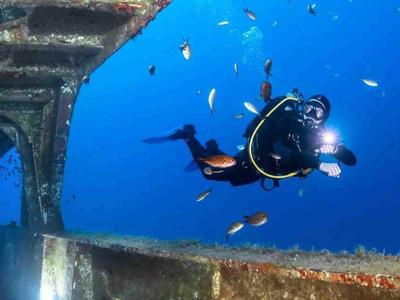 Taucher erkundet ein Schiffswrack unter Wasser mit einer Taschenlampe.
