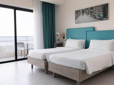 Modern hotelkamer met twee eenpersoonsbedden, balkon en zeezicht.