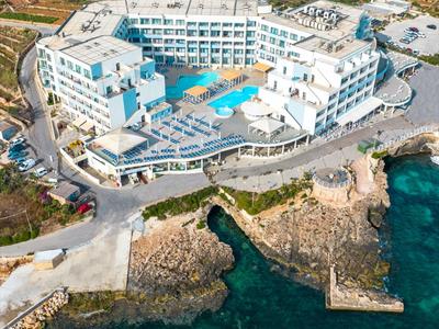 Luftaufnahme eines großen weißen Hotels an der Küste mit Pool und Felsen am Wasser.
