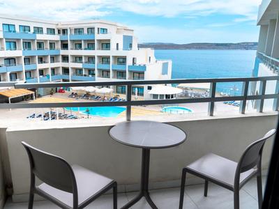 Balkon met tafel en twee stoelen met uitzicht op hotelzwembad en zee op de achtergrond.
