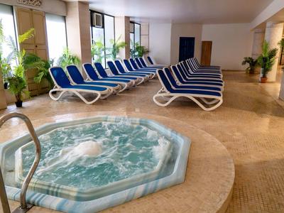 Binnenruimte met een whirlpool en blauwe ligstoelen bij grote ramen.