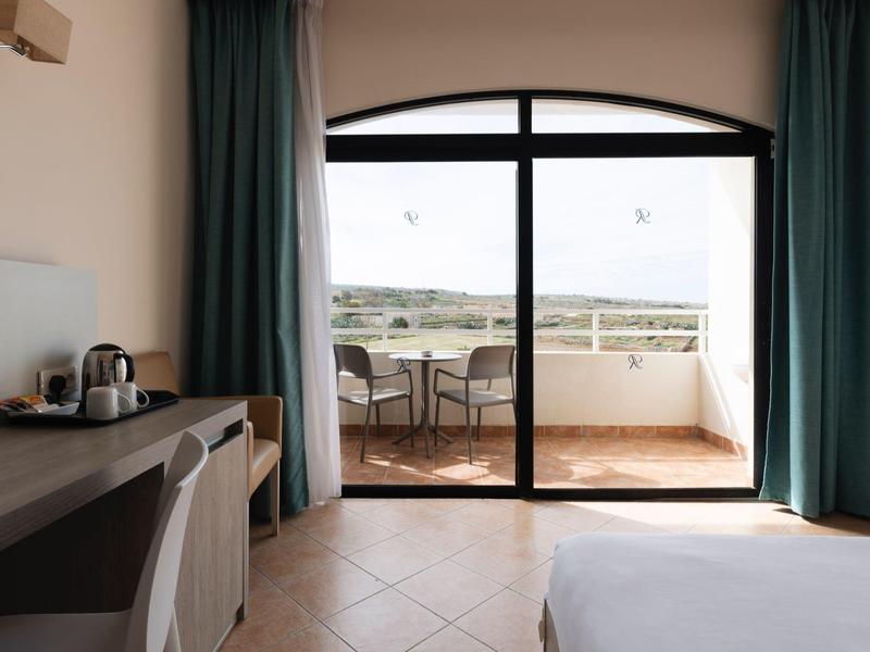 Hotelkamer met bed, bureau, koffiemachine en balkon met uitzicht op een landschap.