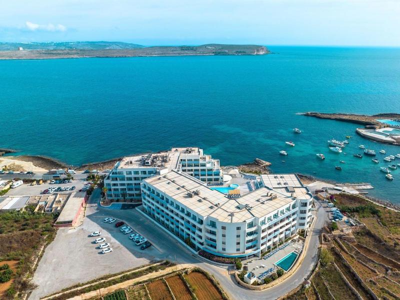 Groot wit hotel aan zee met uitzicht op haven en kustlijn.