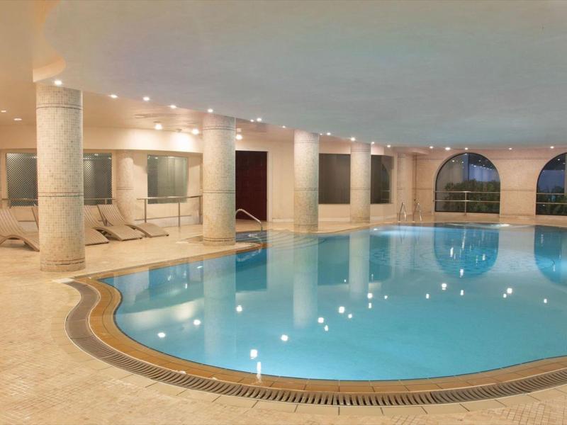 Overdekt zwembad met afgeronde vorm, zuilen en grote ramen in een luxe hotel.