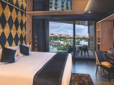 Modern hotel room with large bed, seating area, and city view through large windows.