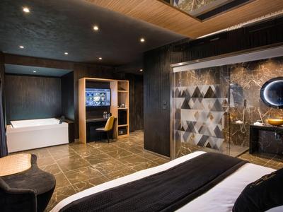 Habitación de hotel moderna con cama, bañera, área de trabajo e iluminación elegante.