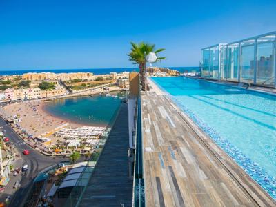 Rooftop hotel pool overlooking a busy coastal promenade and beach.