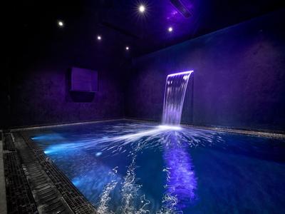 Dark wellness room with illuminated indoor pool and waterfall wall.