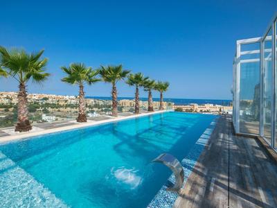 Piscina exterior moderna con palmeras y vistas al mar bajo un cielo azul claro