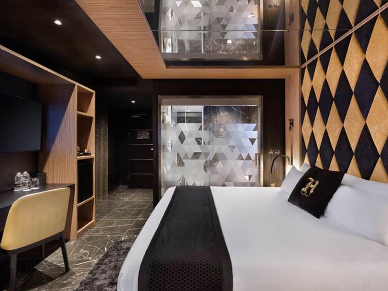Modern hotel room with large bed, desk, and stylish wall decoration in dark tones.