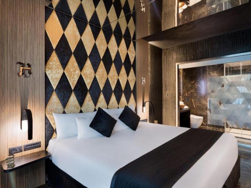 Modern hotel room with large bed, decorative pillows, and diamond-patterned wall decor.