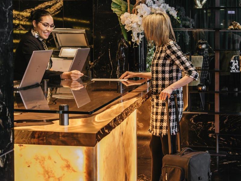 Hotel staff at an elegant, illuminated reception desk attending to traveler with luggage.