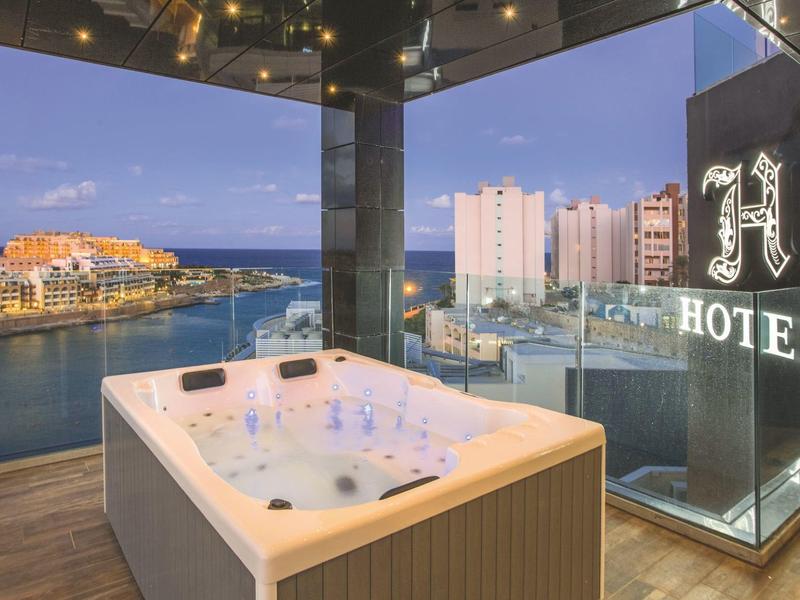 Hot tub on a balcony with sea view and hotel buildings in the background.