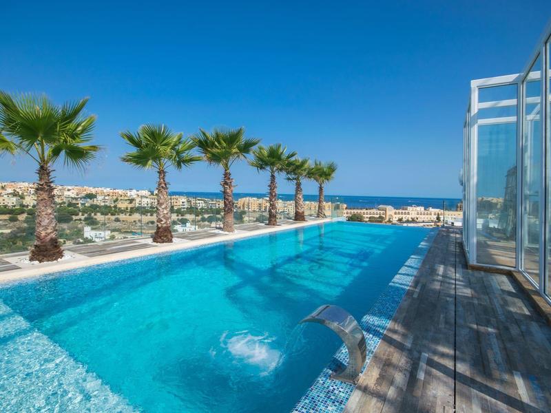 Modern pool with palm trees and sea view under clear blue sky.