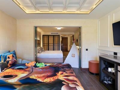 Moderní hotelový pokoj s velkou postelí, barevným kobercem a stanem pro děti