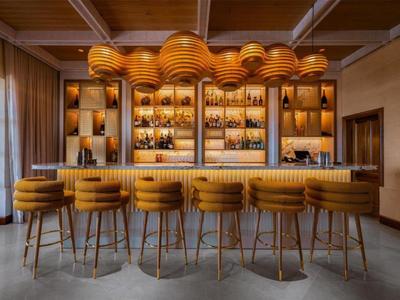 Elegantní hotelový bar se žlutými barovými židlemi a moderním stropním osvětlením.